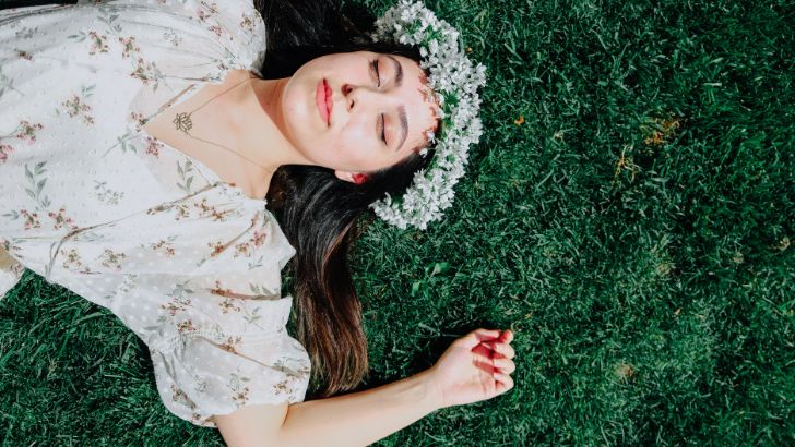 白い花輪をかぶって芝生の上に横たわる女性