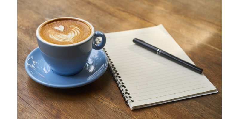 テーブルの上にコーヒーとノートとペン