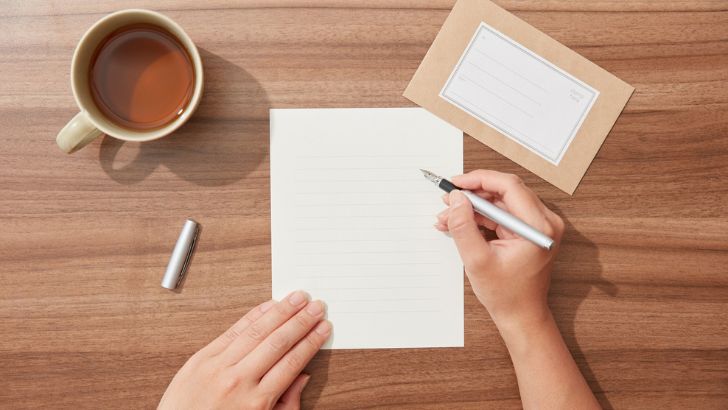 テーブルにカップを置いて手紙を書いている人