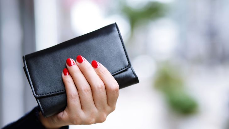 赤いネイルの女性が黒い長財布を持っている